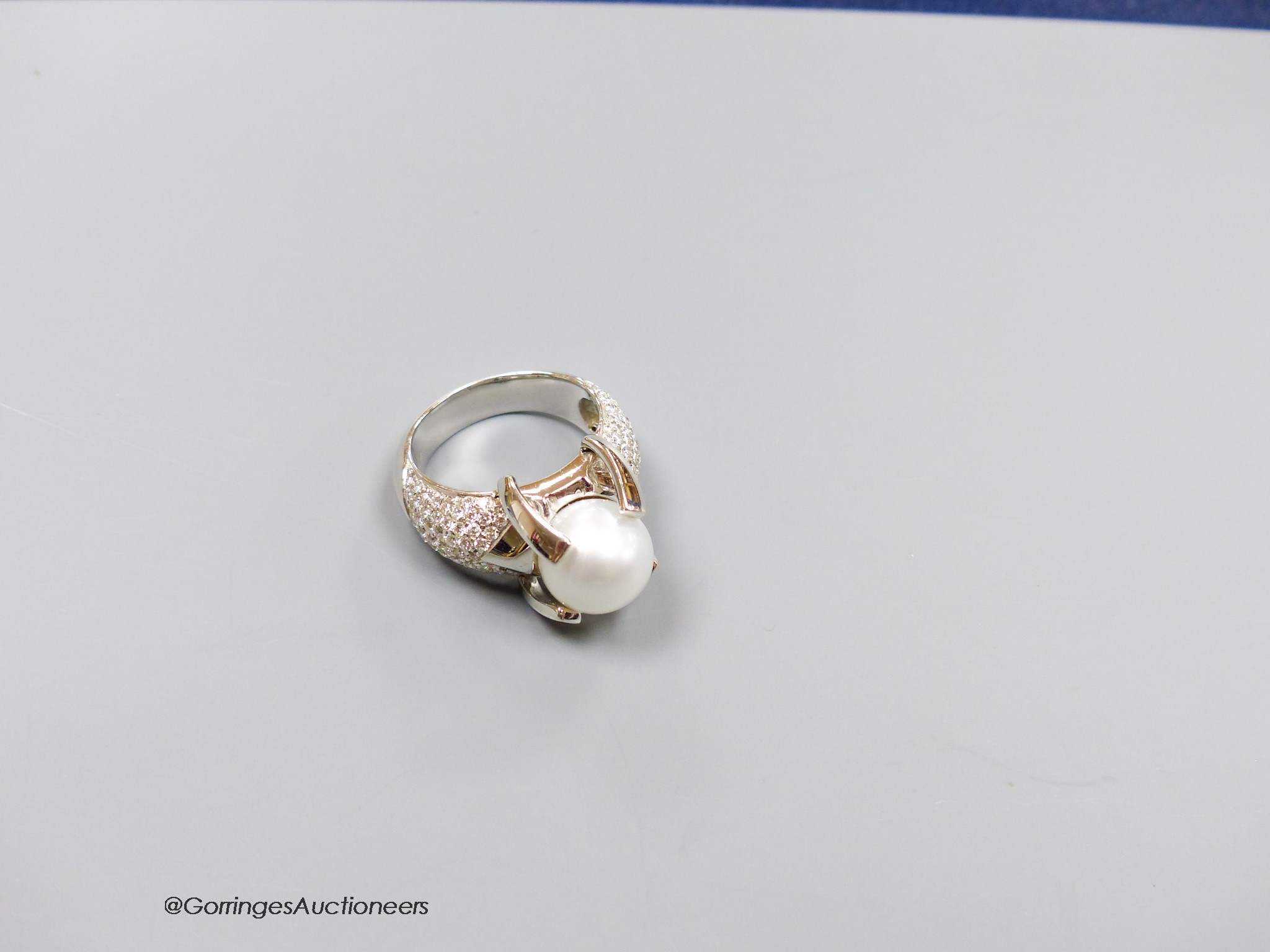 A modern white metal (stamped 750) and claw set cultured pearl dress ring, with pave diamond set shoulders, size R, gross 17.6 grams.